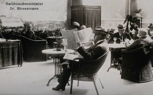 view Baden-Baden, Germany: Gustav Stresemann sitting on the terrace of a grape-cure establishment, reading the newspapers. Photographic postcard, 192-.