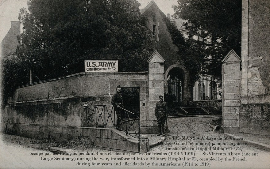 The Abbaye de Saint Vincent transformed into a military hospital in Le Mans, France; two soldiers in the foreground. Photographic postcard, 1920.