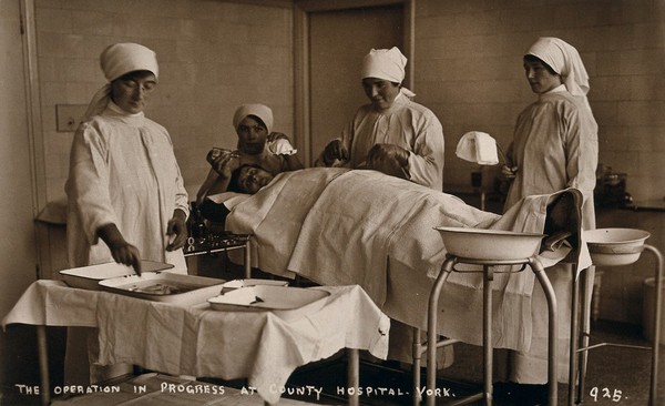 York, England: nurses and patient in the operating theatre of the York County Hospital. Photographic postcard, ca. 1915.