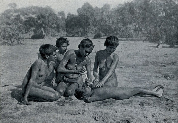 A woman from the Kaytetye tribe is knocking a girl's tooth out with a stone. Halftone.