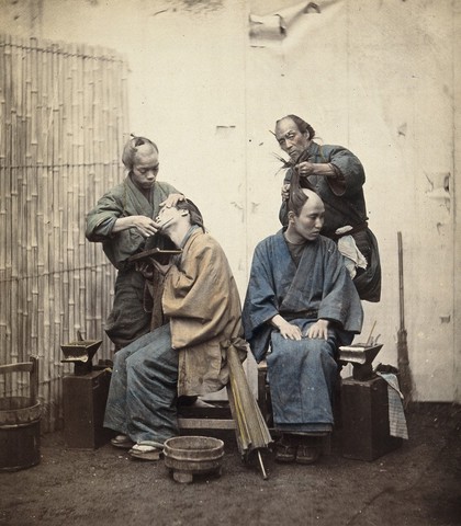 Two Japanese barbers: shaving (left), and hairdressing (right). Coloured photograph.