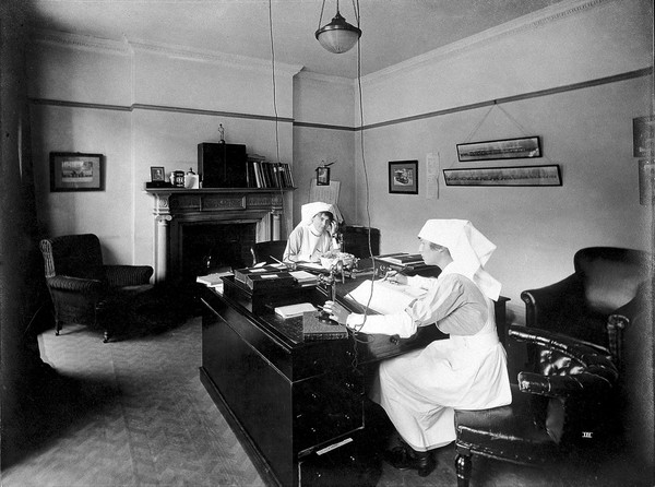 Ambulance Column depot, 9 Gower Street, London: the Record Room, with two women answering the telephone and writing in registers. Photograph, September 1918.