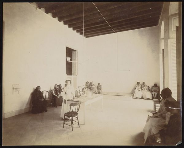 Waiting room in a dispensary for the treatment of tuberculosis, Cuba: a nurse stands beside the reception table, surrounded by seated patients. Photograph, 1902.