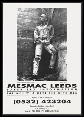 A man dressed in torn denim jeans and jacket stands against a brick wall with his hand inside his trousers; advertisement for Mesmac Leeds. Lithograph , 1990.