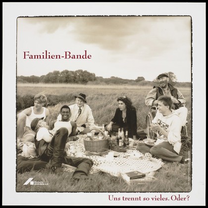 A group of gay men including a transvestite, a black man and a man in a wheelchair sit having a picnic on a check blanket in a field with the message: "Familien-Bande"; an advertisement for the support services for all those affected by AIDS by the Deutsche AIDS-Hilfe e.V. Colour lithograph by Michael Taubenheim and Wolfgang Mudra.