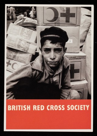 [British Red Cross Society greetings card of a poster featuring a boy in a cap against a pile of Red Cross / Red Crescent parcels].