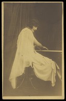 view A man wearing a white dress sits playing the piano. Photographic postcard, 192-.