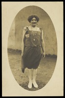 view An amateur actor in drag, wearing a flapper dress and white footwear. Photographic postcard, 1925-1928.