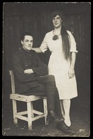 view Two prisoners of war, one in drag, pose with a chair. Photographic postcard, 191-.