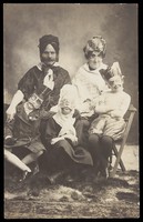 view A family, all members wearing grotesque masks, the father in drag. Photographic postcard, ca. 1910.