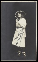 view An amateur actor in drag, posing as 'Ninon', wearing a white dress and hat. Photographic postcard, 192-.