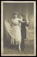 view Two actors, one in drag, dancing together on stage. Photographic postcard, 1918.