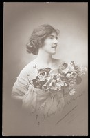 view Eddie Edwards, an actor in drag, wearing a white fabric robe, holding a bouquet of flowers. Photographic postcard by L.E. Muller, 191-.