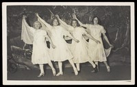 view Amateur actors in drag, wearing white dresses and dancing on stage. Photographic postcard, 191-.