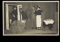 view Amateur actors, one in drag, perform a scene on stage. Photographic postcard, 191-.