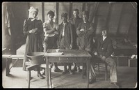 view French prisoners of war, one in drag, gather round a small wooden table. Photographic postcard, 191-.