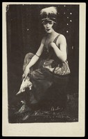 view Chris Bennett in drag sits on stage, wearing a feathered head garment. Process print, 1921.