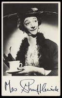 view Mrs. Shufflewick (Rex Jameson), in drag character, holding a cup of tea. Photograph, ca. 1955.