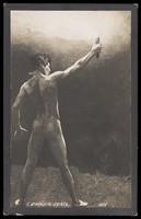 view A naked man holds aloft a torch to illuminate a monster. Photographic postcard by S. Schneider after a drawing, ca. 1910.