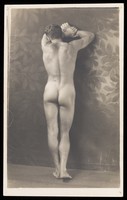 view A naked model, possibly Laurence Woodford, leaning against a painted backdrop. Photographic postcard, 19--.