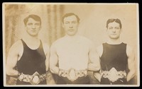 view Three male wrestlers posing with champion belts. Photographic postcard, 19--.