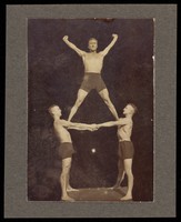 view Three male acrobats perform a human-pyramid. Photograph, 19--.