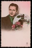 view A man holding the shape of a heart decorated with roses and holly. Coloured photographic postcard, 193-.