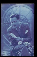view A young man seated holding flowers and a note. Colour photographic postcard, 192-.