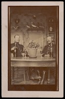 view Two military officers in uniform sitting at a table in a domestic kitchen. Photographic postcard, 191-.