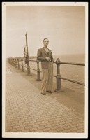 view A man with a cigarette posing on a promenade by the sea. Colour photographic postcard by Jerome Ltd., 192-.