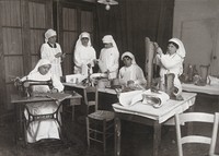 view Artificial limb factory in Rome: six women working at benches, one using a sewing machine and one stitching the back of a full-length leg. Photograph, 1914/1918.