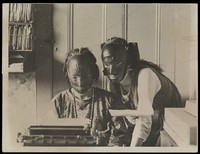 view Rubber beauty masks, worn to remove wrinkles and blemishes; modelled by two women at a typewriter. Photograph, ca. 1921.