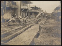 view Colón, Panama: men construct sewers in the middle of a road lined with wooden houses, as part of a programme of sanitary work implemented during the construction of the Panama Canal. Photograph, 1910.