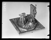 view Photograph of scientific apparatus referenced as "Base plate and film holder support - back step tube and collinator stand for tilting micro camera"