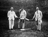 view M0005204: J. W. Scharff (left) and two unidentified men holding a drain penetrated by roots